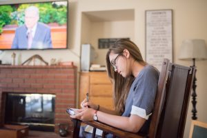 young woman taking notes while watching general conference