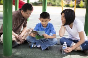 father and mother reading with child at the playground